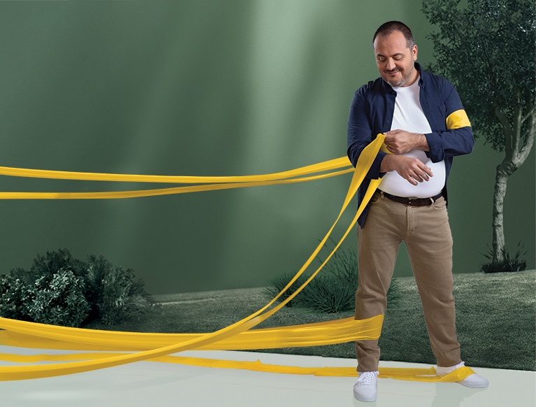 Um homem com obesidade, num parque, a remover as faixas de resistência dos seus braços, enquanto continua a ter as faixas à volta das pernas.